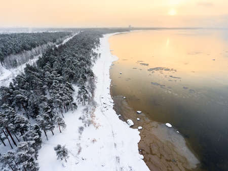 Winter sunset on the Baltic sea, snow covered sandy beach line, evergreen trees and open water, the Gulf of Finland, St. Petersburg, Russiaの写真素材