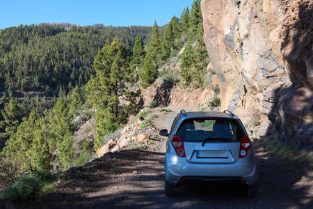 Small car standing in shadow from trees on dirt mountain country road, travel by car over the...