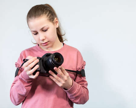 Teenage Caucasian girl looking at new big DSLR camera, first-timer in photography, a grey background, copyspaceの写真素材