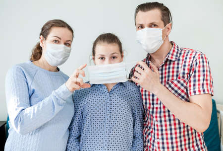 Parents dress medical mask on face of teenage daughter, father and mother wearing facial mask, domestic roomの写真素材