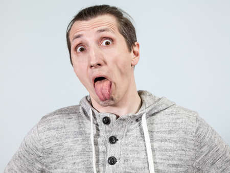 Crazy man showing his tongue with wide opened eyes, a grey backgroundの写真素材