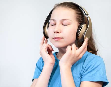 Caucasian young girl listening music wearing wireless headphones, closed eyes, blue t-shirt, grey backgroundの写真素材