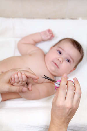 Human hand with scissors cutting baby nails on arms, scared infant lying on his backの写真素材