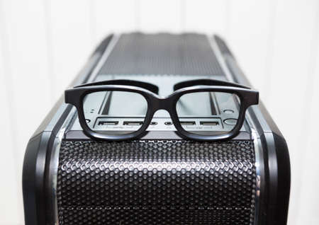 An eyeglasses is on top of black pc tower case with usb connection sockets, power and reset buttons, close-up viewの写真素材