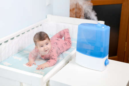 Using humidifier for prevent pulmonary disease, Caucasian infant child lying in cot next to ultrasonic deviceの写真素材