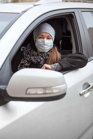 Attractive adult woman wearing protective mask sits inside her car on driver seatの写真素材