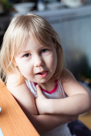 Portrait of little girl sitting at the table with crossed arms, cheerful and funny Caucasian kid