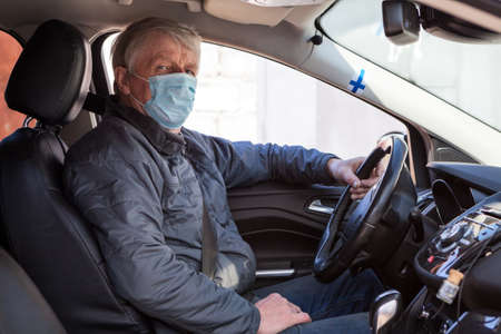 An elder Finn man sitting inside car wearing protective mask, prevention of a virus infectionの写真素材