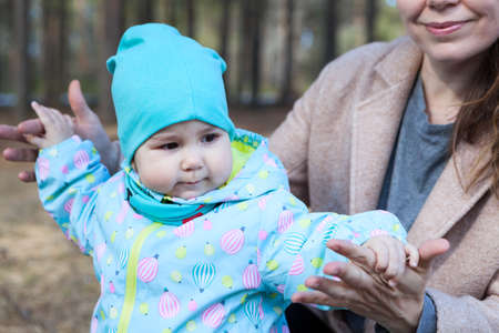 Toddler child stepping with mother support, female hands holding child, outdoorsの写真素材