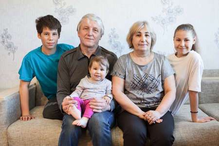 Senior couple with teen age grandchildren and infant granddaughter portrait, sitting on a couch at homeの写真素材
