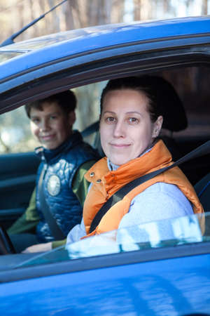 Two Caucasian smiling people sitting in car, looking at camera