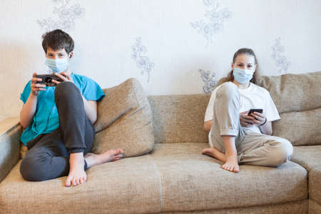 Portrait of two preteen kids sitting at the distance on a couch at home, holding cellphonesの写真素材
