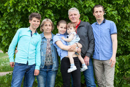 Six people Caucasian family portrait against a green tree, elderly grandparents, adult single...
