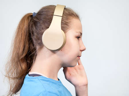 Wireless headphones is on head of Caucasian teenage girl, side view, a grey background