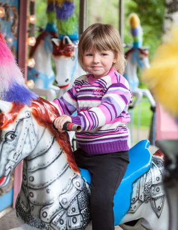 Adorable little kid girl riding on a merry-go-round carousel horse at funfair or market, outdoors. Happy Caucasian child having funの写真素材