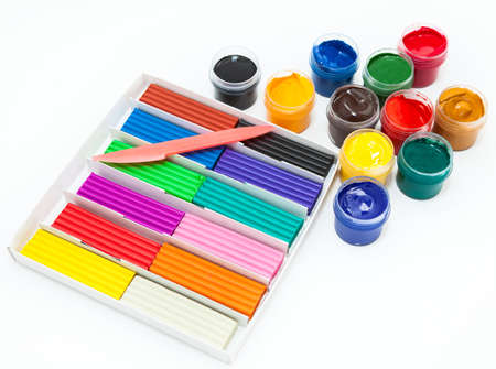 Cardboard box with colorful plasticine bars, plastic knife and color paints in bottles, a white...