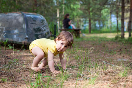 Little child trying to stand up while walking barefoot in evergreen forest with her mother, summer seasonの写真素材