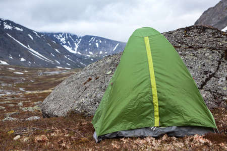 Green waterproof and windproof tent for hiking is in mountains at windy weather, standing behind big stone for protection from the wind, copy spaceの写真素材