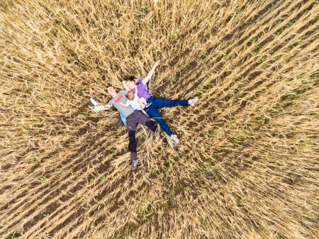Father, mother and toddler daughter lying back on dry wheat field, top view from drone, quadcopter...
