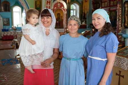 Russian women before toddler baptism are in church, godmother with goddaughter, mother with teenager daughter, indoors portraitの写真素材