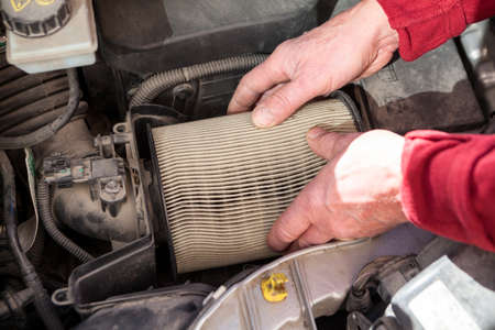 Mechanic hands taking out dirty air cartridge from airbox of car engine, close-up viewの写真素材