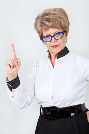 Caucasian senior woman pointing with forefinger, elderly lady wearing eyeglasses is on grey backgroundの写真素材