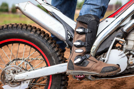 Close-up view at rider's motocross boot standing on peg of dirt motorcycle. Safety apparel for ridingの写真素材