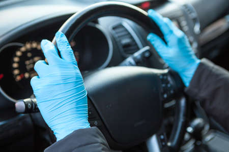 Human hands in blue medical gloves holding steering wheel. Protection against the Covid-19 virus,...