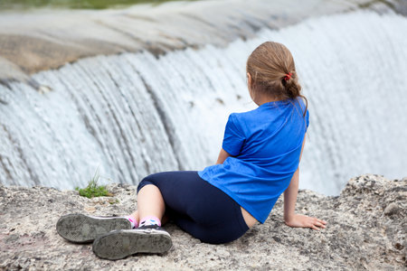 Rear view at preteen age girl sitting on edge of waterfall of the Cijevna river. It is called Montenegrin Niagara Falls. Surroundings of the Podgorica city. Montenegro, Europeの写真素材