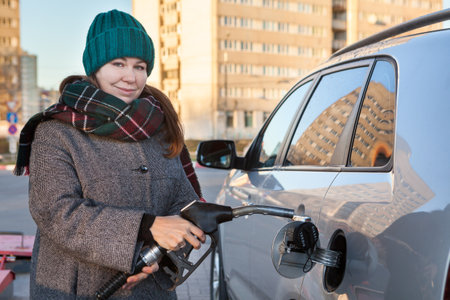 Smiling woman insertin nozzle in tank for refueling a car at a petrol stationの写真素材