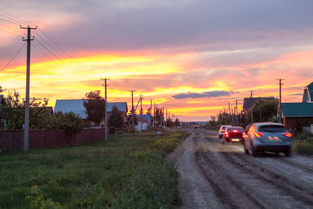 Passenger cars driving on a rural road in village at sundown, Russiaの写真素材
