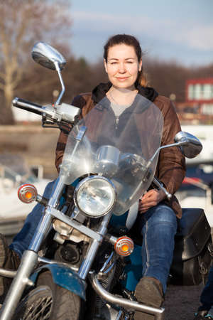 Caucasian woman with her motorcycle, sunlight, front view, looking at cameraの写真素材