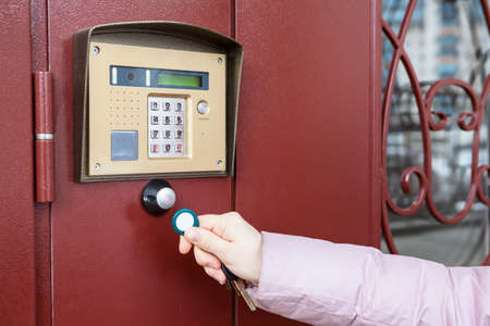 Person with wireless key touching intercom for house access, close up view