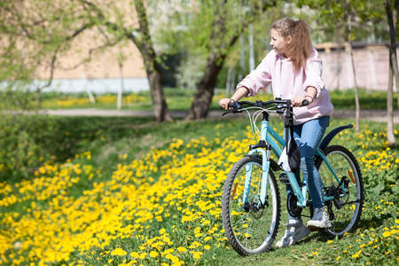Teenager Caucasian girl riding bicycle in spring park with yellow flowersの写真素材
