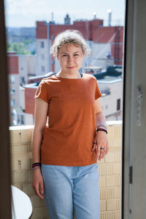 Happy teenage girl standing on balcony, looking at camera. Shoot through the door opening. Caucasian child with curly hairsの写真素材