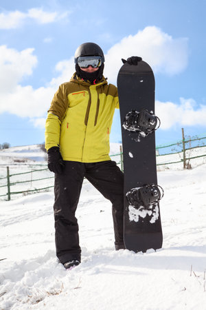 Adult snowboarder in a winter helmet and protective glasses dressed in a snowboarding coat posing with a snowboard outdoors, looking at a cameraの写真素材