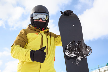 Snowboard and snowboarder with thumb up. Man wearing helmet, goggles and gloves. extreme winter sportsの写真素材