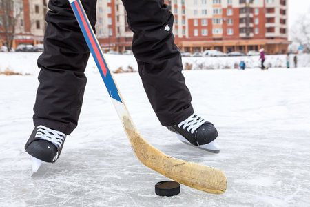 Forward holding black puck with stick, hockey skates on a lake ice, teenage male legs, front viewの写真素材