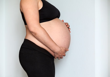 Side view at pregnant Caucasian woman with big belly, female holding hands her abdomenの写真素材