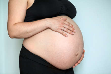 Caucasian pregnant woman with large belly, female holding hands her bodyの写真素材