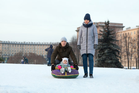 Caucasian family with winter tubing toboggan, father push her child from snowy slopeの写真素材