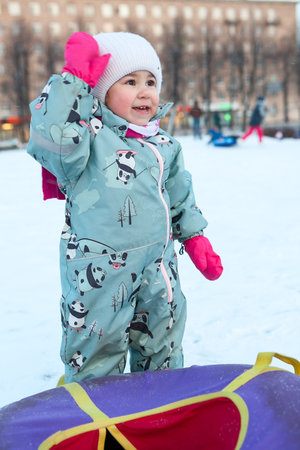 Little frozen girl is ready for riding on snow tubing from slope in city parkの写真素材