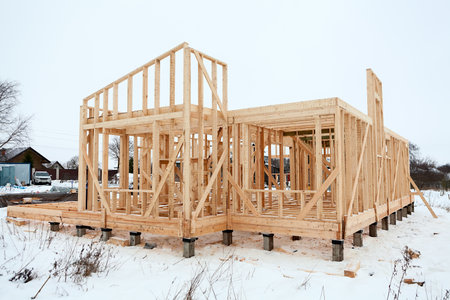Wood frame house under construction, bare frame and walls with pile foundation, winter season