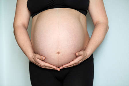 Front view at pregnant woman with big belly, female holding hands her abdomen