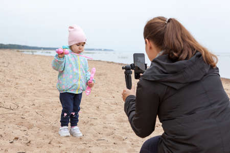 Rear view of mother taking picture with her small daughter playing soap bubbles on empty sandy beachの写真素材
