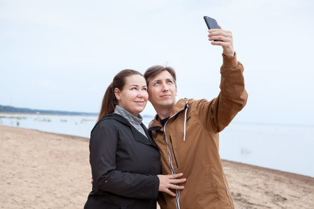 Loving cheerful happy couple taking selfie at the sandy beach against the seaの写真素材