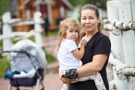 Young mother holding hands her heavy two years old daughter, woman love to her child, countryside portraitの写真素材