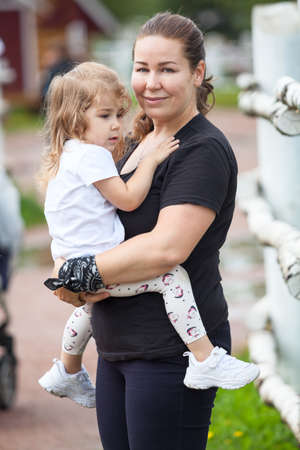 Mother and daughter portrait embracing together, female carrying her little child on hands, two Caucasian peopleの写真素材