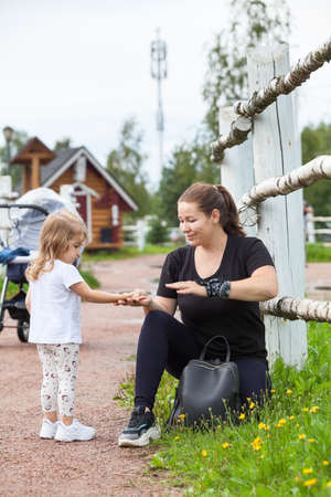 Mother holding hand of her small daughter and talking, family walking in village with baby strollerの写真素材