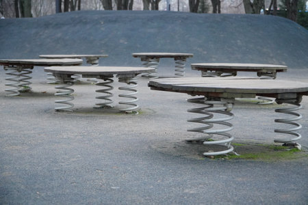 Row of vintage spring-mounted circular bouncers on concrete playground surface with large metal coil springs under wooden seats designed for children jumping play in outdoor public parkの写真素材